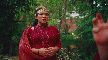 Partial view of a person in traditional red attire with intricate patterns, standing amidst lush greenery. video