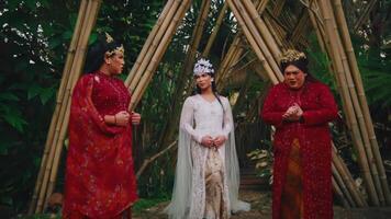 Three people in traditional attire standing in a garden with bamboo structures. video