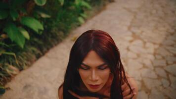 Portrait of a woman with red hair and makeup looking downward, set against a blurred background of a cobblestone path. video