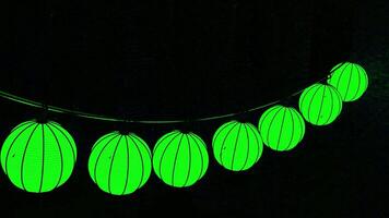 Halloween pumpkin garland hanging isolated on a black background. Design. Unusual green lanterns in a form of a pumpkin swaying in the wind under the rain drops. video