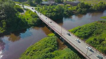 A bird's-eye view of summer. Clip. The bridge on which cars drive over the river, next to which there is a forest behind forests and fields and blue summer. video