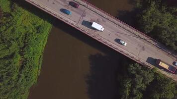 A small bridge over the river. Clip. The view from the drone. A narrow river through which there is a high bridge on which cars drive next to green grass and trees . video