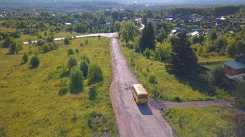 yeux d'oiseau voir. agrafe. une longue route sur lequel une Jaune autobus monte contre une Contexte de vert des arbres et herbe video