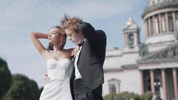 Beautiful newlyweds on background of old architecture. Action. Elegant couple of newlyweds posing on background of cathedral on sunny day. Newlyweds on windy sunny day in summer video