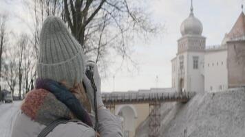 uma mulher dentro caloroso roupas levando As fotos do lindo inverno velho cidade arquitetura em uma Câmera. Ação. conceito do turismo e viajando. video