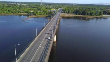 View from the height . Clip. A large long bridge over the river on which cars drive and there are lights behind the bridge you can see a green city with small residential buildings and a large forest video