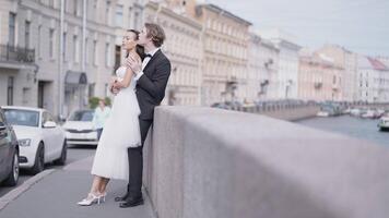 Side view of caring lovely just married couple embracing by the granite sidewalk. Action. Elegant bride and groom outdoors in the street. video