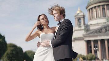 Beautiful newlyweds on background of old architecture. Action. Elegant couple of newlyweds posing on background of cathedral on sunny day. Newlyweds on windy sunny day in summer video