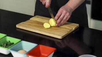 een Mens snijdend een geschild aardappel Aan een houten bord. kunst. dichtbij omhoog van mannetje chef voorbereidingen treffen een schotel en gebruik makend van een staal mes voor snijdend groenten. video