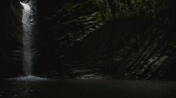 A beautiful mountain in which there is a small waterfall. Creative. A girl standing washing her face and drinking clean water in a cave through which a stream flows from a stream that runs in the cave video