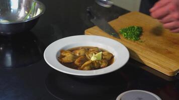 Cook serves dumplings in a white plate.ART. The cook's hands close-up add butter and green onions to the dish video