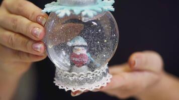 le fille se tourne plus de une verre Balle avec neige dans sa mains. art. à l'intérieur le neige globe est une manchot avec une cœur dans une écharpe video