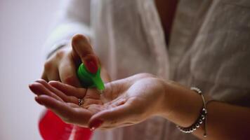 A woman squeezes liquid from a vial onto her hand. ART. Colored jar and woman's hands close-up.Woman uses disinfectant during a pandemic video