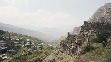 Ruins of ancient village with abandoned building stone walls on a mountain slope. Action. Summer cliff and residential settlement near the rock on cloudy sky background. video