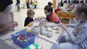 Norvegia, Oslo - marzo 17, 2022. bambini scolpire figurine a partire dal argilla. arte. ragazzo e ragazza con loro madre siamo apprendimento Come per rendere giocattoli a partire dal crudo argilla. donna insegna sua studenti ceramica artigianato video