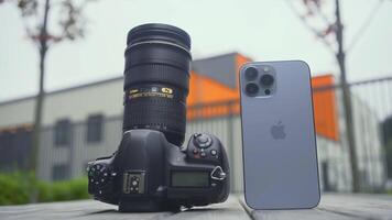 RUSSIA, MOSCOW - SEPTEMBER 27, 2021. Camera and phone comparison. Action. Professional camera with lens or new iPhone. Comparison of cameras of new iPhone 13 pro with professional camera video