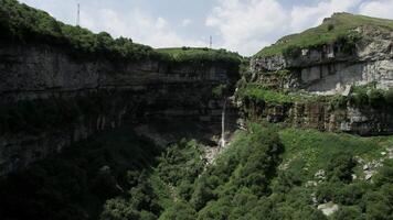 aereo Visualizza al di sopra di sbalorditivo naturale paesaggio con estate enorme roccia formazioni e un' cascata. azione. volante sopra verde versante coperto di erba e alberi. video