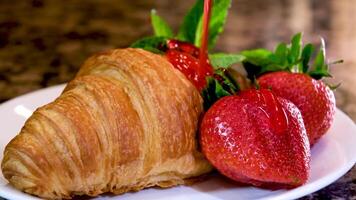 sur une blanc assiette fraise menthe et une croissant avec fraise liquide sirop verser délicieux des pâtisseries écoulement vers le bas sur une assiette avec longue gouttes délicieux dessert Contexte pour tout spectacle panneau d'affichage video