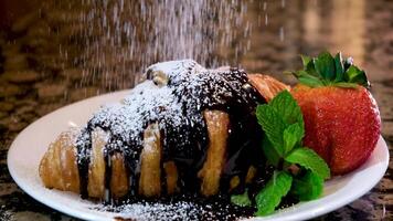 molte di buio cioccolato versato su brioche cosparso con in polvere zucchero menta fragola su bianca piatto e pietra marmo tavolo dolce servendo delizioso cibo ristorante francese servendo fatto a casa video