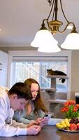 adolescentes en el cocina comiendo Fruta jugando en teléfono blanco mueble acogedor hogar comunicación cosecha un uva desde un plato con manzanas y bananas flores fiesta ordinario día en Canadá video