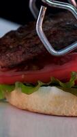 Step by step cooking a burger juicy fried cutlet, fresh lettuce, thin slice of cheese, onion and tomato next to French fries and sauce in a glass Cup. Kitchen in the background. video