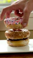 two hands put delicious donuts on a white plate three different Donuts with holes pink chocolate and glazed close-up offer menu tasting dessert large selection advertising video