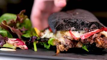 un mujer mano toma un enorme mordido hamburguesa desde un negro Roca plato para comida ensalada de cerca delicioso comida negro bollo video