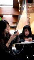 jung asiatisch Mädchen Sitzung im ein Cafe beim ein Tabelle mit Handy, Mobiltelefon Telefone Smartphones Neu Generation von Kommunikation auf Internet finden W-lan Nein Leben Kommunikation Sucht zu Gadgets Leben im Ihre besitzen Welt video