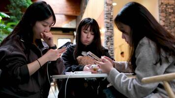 young Asian girls sitting in a cafe at a table with mobile phones smartphones New generation of communication on Internet find wi-fi No live communication addiction to gadgets live in your own world video