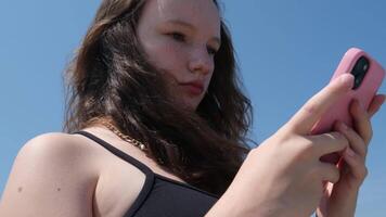 tournage de au dessous de contre le ciel adolescente enfant en utilisant téléphone intelligent dans parc, adolescent fille avec école sac navigation l'Internet sur intelligent téléphone les enfants en jouant dispositifs video