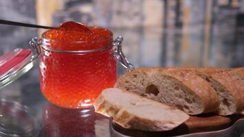 Open tin can with red caviar on background. The hand holds a spoon and takes out red caviar from a jar video