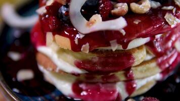 stack of delicious pancake decorated with coconut flakes blueberries hazelnuts almond flakes raspberries and jam delicious breakfast with sour cream eaten with fork in restaurant beautiful serving video