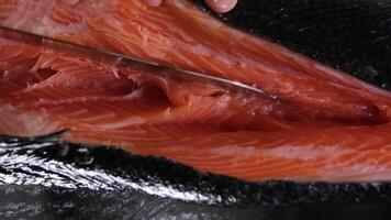 con un' acuto coltello tagliare via grande pezzi di rosso pesce salato salmone cucinando per Sushi a casa lento movimento video