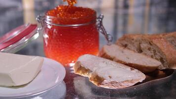 een meisje maakt boterhammen met rood kaviaar vis kaviaar rijkdom van luxe Aan een transparant tafel. zwart achtergrond plak brood video