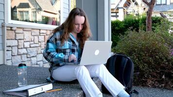Adolescência menina com uma computador portátil sentado em a varanda do a casa. ela assistindo a notícia fazendo dever de casa conectados conferência mochila pasta água garrafa lápis comum pessoas real vida video
