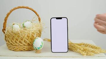 Pâques vacances téléphone avec blanc Contexte panier des œufs avec brodé modèle ruban spectacle pouce en haut coquilles d'œufs blé épillets sur table endroit pour pâte fermer panier à église blanc écran video