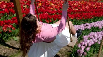 un' ragazza giocando nel un' fiore giardino cavalcata su un' swing capelli si sviluppa rosa camicetta di un' europeo ragazza bianca gonna video