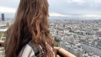 A girl on a eiffel tower looks around at the city of Paris visible houses the Seine River with boats and the city center Paris France video