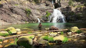 handsome sexy dark-haired man like Tarzan comes out of a mountain river near a waterfall footage as if from an adventure movie video