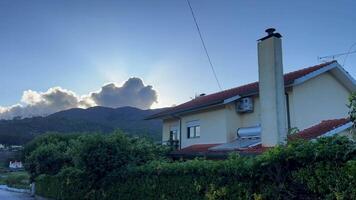 White house with a red roof in the mountains against the backdrop of a huge cloud over the mountain the sun illuminates the cloud counterfoil video