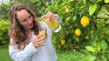 Está somente uma limão paraíso, uma Adolescência menina carrinhos contra a pano de fundo do uma limão árvore com limões e bebidas limonada a partir de uma vidro vidro dentro dela de outros mão, ela detém uma jarro do beber video