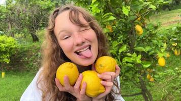 niña adolescente tener divertido bailando sonrisas y se ríe en contra el fondo de un limón árbol en su manos ella tiene limones ella tontos alrededor con ellos video