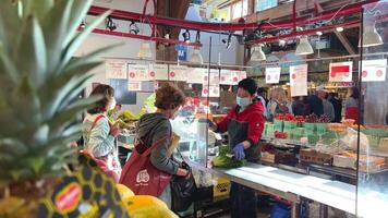 Trois femmes sont vu dans le marché une femme vendeur dans une masque packs une salade dans une Plastique sac 2 femmes supporter dans ligne dans de face de un de leur prend sa sac est le acheteur masque mode tout dans masques video