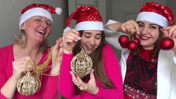Frauen Tanzen drei Frauen sind feiern das Neu Jahr, Sie sind tragen ein rot Hut mit Schneeflocken im ihr Hände Weihnachten Baum Spielzeuge Party Kommunikation Liebe Freundschaft Haus Party während Quarantäne video