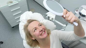 beautiful young middle-aged woman admiring herself in mirror in dental chair after whitening procedure latest technology Medical secret beauty grooming sterility joy of patient satisfied person video