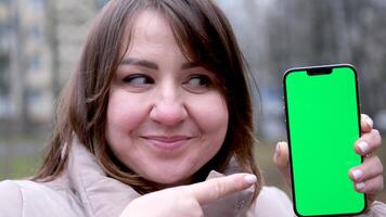 Over shoulder view of female person holding and pressing on smartphone with mockup screen while sitting at street. Concept of chroma key and greenscreen video