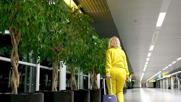 arriving or departing at airport woman with suitcase on wheels in hands hand luggage communication waiting night outside window walk down corridor middle-aged blonde real people Amsterdam airport video