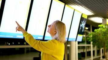 een vrouw looks Bij de scorebord op zoek voor haar vlak van de schema van vliegtuigen wit ruimte voor tekst helder pak luchthaven spoorweg station aan het wachten handig technologie video