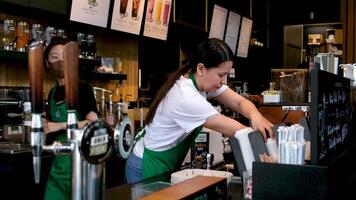 Starbucks preparing coffee of various drinks behind counter women white t-shirt aprons and masked sellers in glasses of Asian-European ethnicity girl peeking in to take coffee latte showcase issuance video