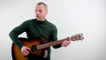 handsome man with a beard plays beautiful melody on an acoustic guitar. White background. Isolated. Medium long shot video